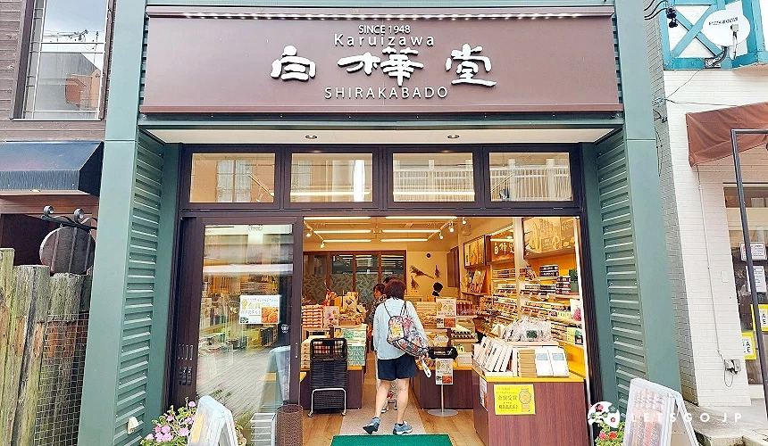 位於輕井澤的白樺堂 (SHIRAKABADO) 店面,深棕色招牌配上白色的品牌字體,門口展示著獲得金賞肯定的伴手禮海報,店內陳列著各式知名點心與甜點