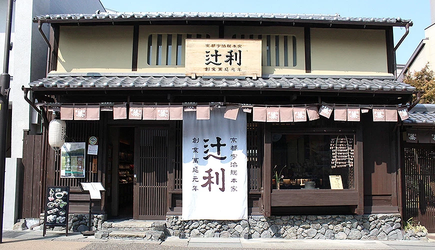 京都宇治總本家辻利茶舖外觀:木造日式町屋建築,屋頂瓦片與木格柵窗,下方懸掛白色暖簾,正上方是書有「辻利」字樣的木製招牌。