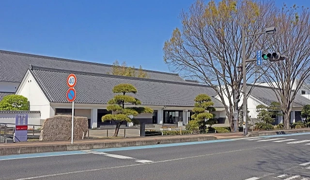 日本埼玉縣川越市立博物館外觀,建築採用黑瓦與白牆的傳統藏造風格設計,前方有植栽造景與馬路邊的交通標誌
