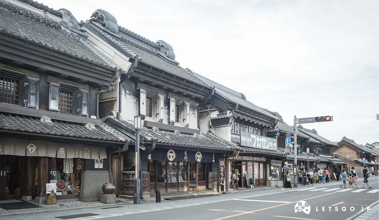 街道兩側排列著黑色木造日式商店建築,行人於路口行走,路口設有紅綠燈