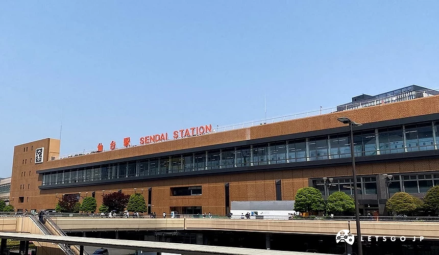 仙台站站體外觀,建築立面掛有「仙台駅 SENDAI STATION」紅字招牌,晴天藍天背景