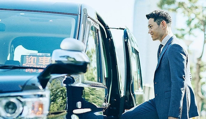 一位穿著西裝的男子微笑著準備搭乘計程車,車門已開啟,畫面呈現專業舒適的乘車體驗