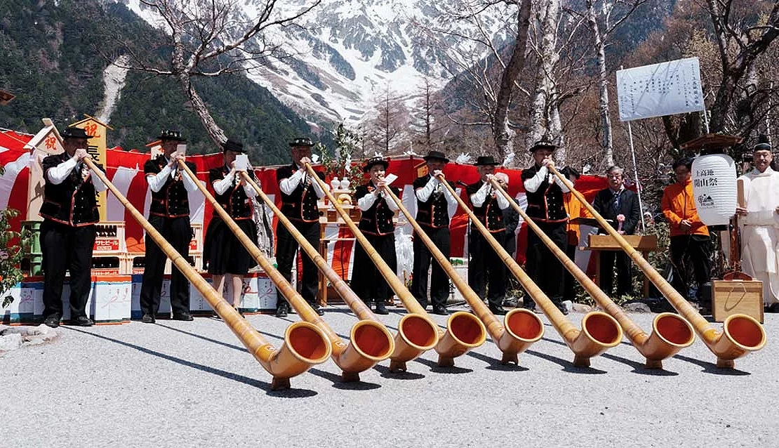 一排人站在雪山前面,穿著傳統服飾,吹著長喇叭