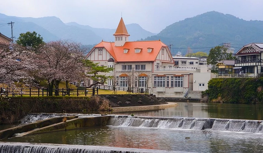 河畔橘色屋頂的溫泉建築前方,小瀑布流過,櫻花點綴河岸