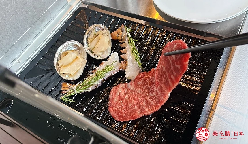 烤盤上正在烤和牛肉片、鮑魚與龍蝦尾,旁邊放有香草枝