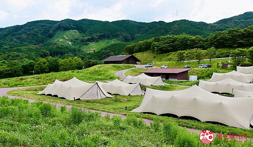 綠色山谷中排列白色帳篷群,後方有木屋與停車場