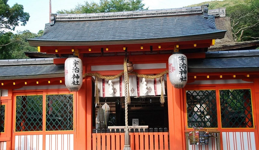 宇治神社正殿入口特寫,橙紅色木門上方垂掛繩結與紙垂飾,兩側紙燈籠標示神社名稱,屋頂為灰黑色瓦片結構。