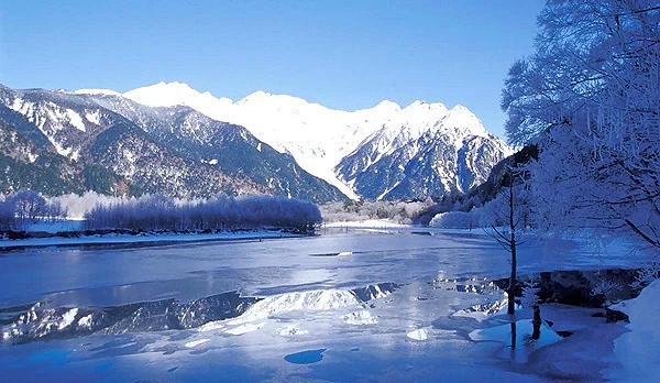白色雪山,前面的溪流結冰,右邊樹枝上有積雪