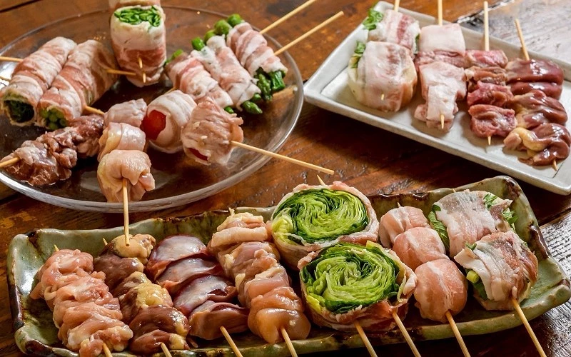 多盤串燒食材擺盤,有培根蔬菜卷、雞肉串與內臟串