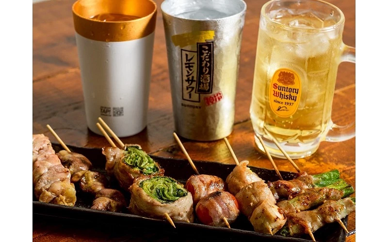 串燒肉串擺放在黑色長盤中,搭配三杯含冰飲品,其中一杯印有 Suntory Whisky 標誌