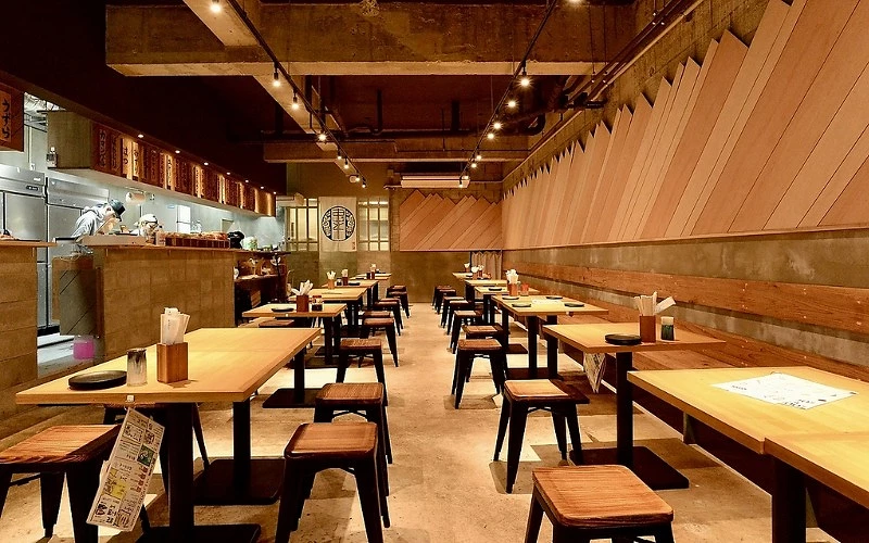 店內整齊排列木桌椅,後方可見廚房與開放式吧檯