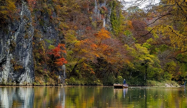 岩手縣猊鼻溪的秋日景色,高聳岩壁與楓紅倒映溪水,遊船緩緩行駛其間