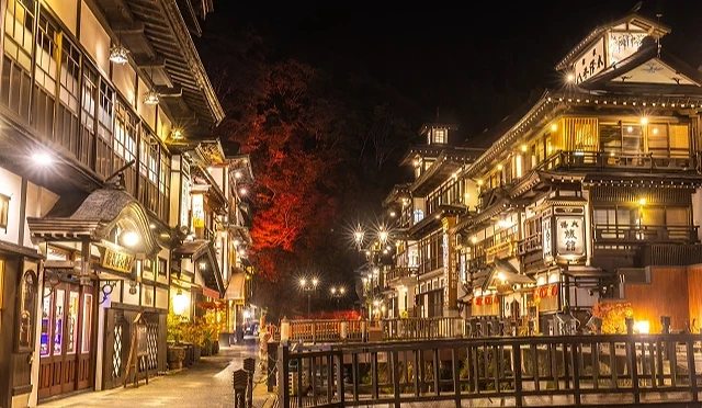山形縣銀山溫泉夜景,復古木造溫泉旅館燈火通明,背景映襯紅葉,氛圍浪漫夢幻