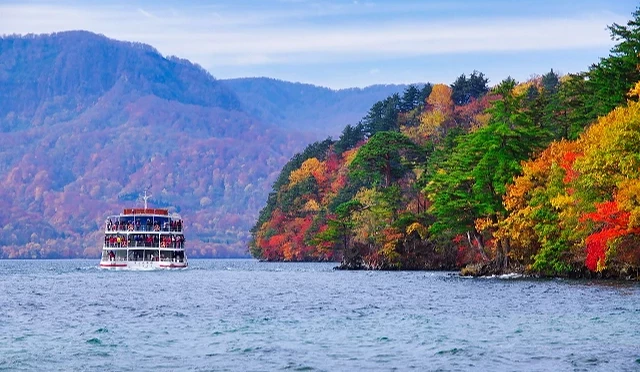 十和田湖遊船航行於碧藍湖面,沿岸楓紅與常綠松樹交織