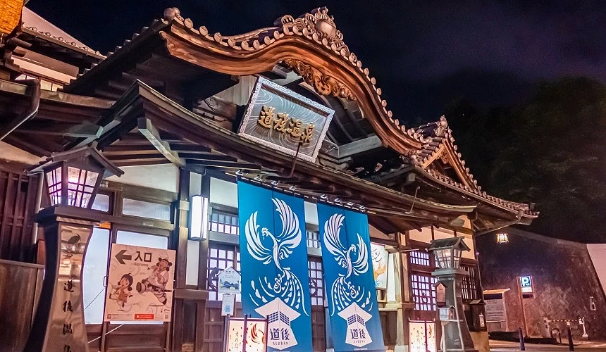 道後溫泉本館夜間景觀,傳統木造建築配上藍色暖簾與鳳凰圖騰