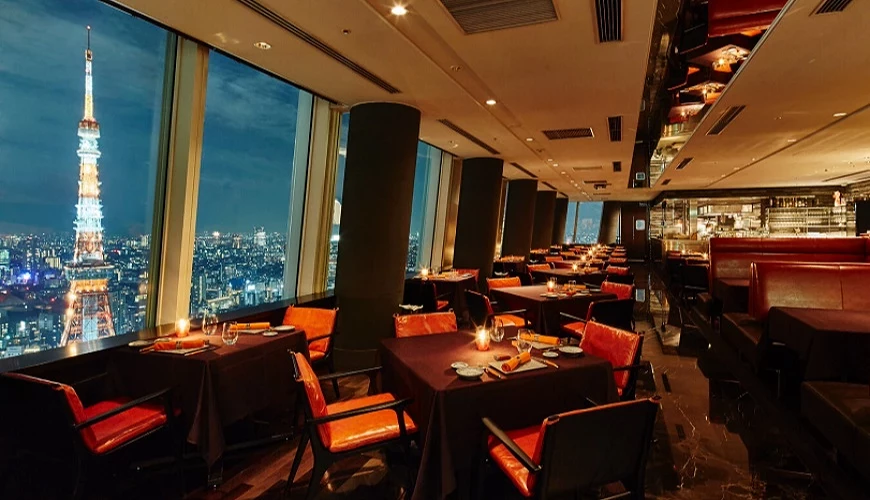 東京鐵塔夜景佐餐景觀餐廳內部,落地窗外可見東京夜景與點燈的東京鐵塔,室內座位典雅舒適,燈光昏黃營造高級氛圍。