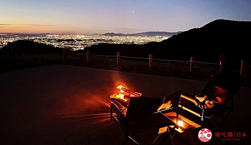 椅旁望夜景,前方有營火與遠處城市燈光