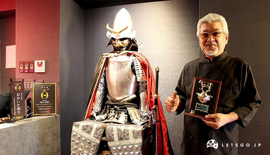 一名男子手持獎牌站在武士盔甲旁,後方展示有大分和牛標誌