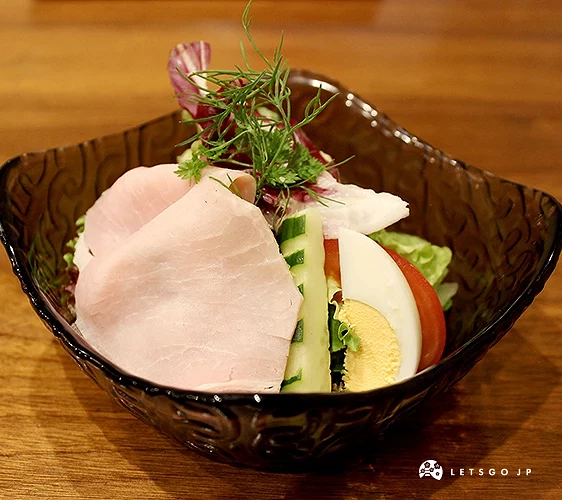 黑色碗中盛有生菜沙拉,搭配火腿片、番茄片與水煮蛋