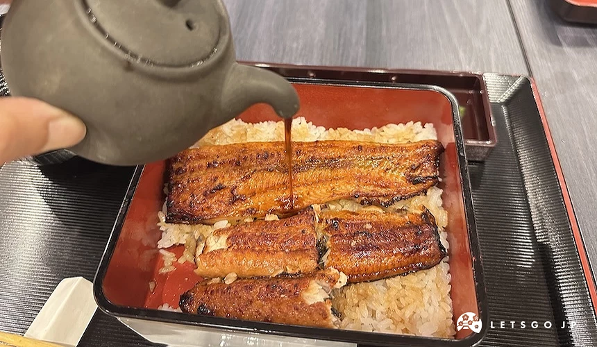 手持茶壺將醬汁淋在餐盒內的烤鰻魚飯上