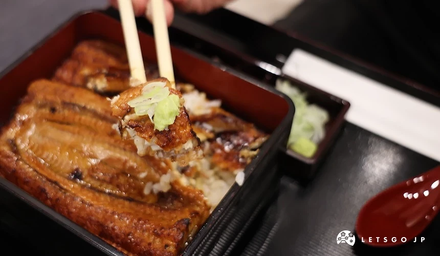 筷子夾起餐盒內的烤鰻魚飯,上方放有蔥花和芥末