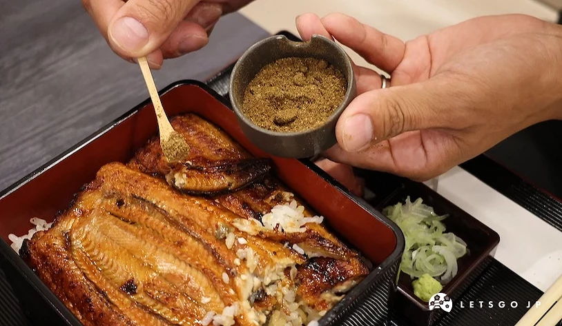 手持小碟將粉末調味料灑在鰻魚飯上