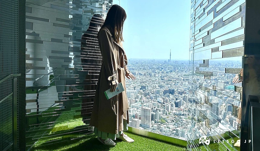 一位女性站在馬賽克鏡子窗旁俯瞰東京城市風景