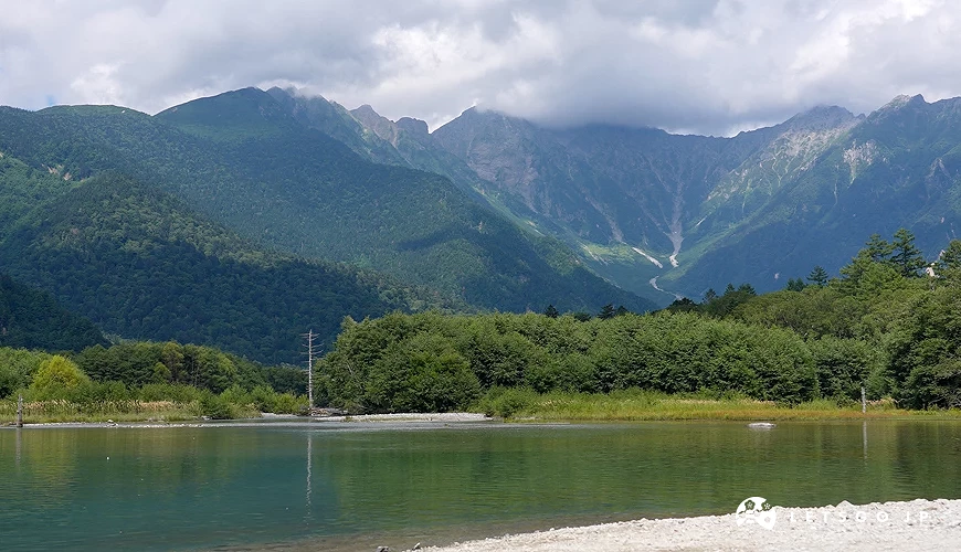 藍天白雲,綠色的山脈,前面是樹林,最前面是一大片池子。