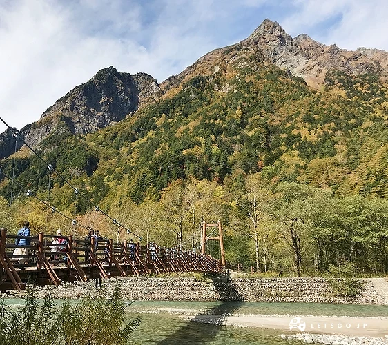 綠色山脈的前面有一座木造橋,橋下有一條溪流