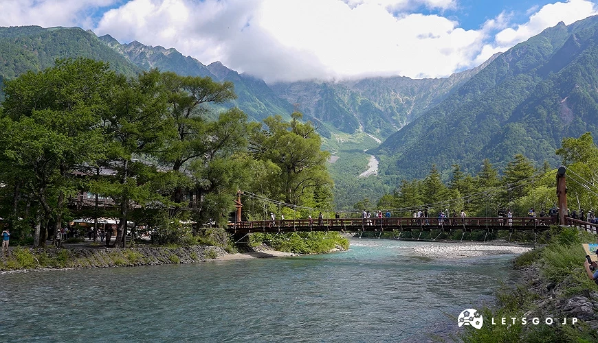後面是山脈,前面有一個吊橋,吊橋下面是一條溪流。