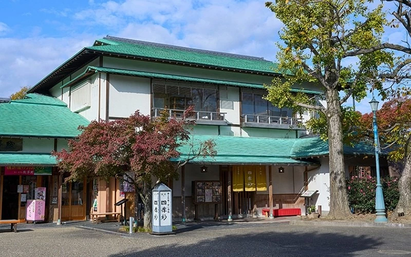 綠色屋頂的日式餐館外觀，前方有樹木與紅色長椅