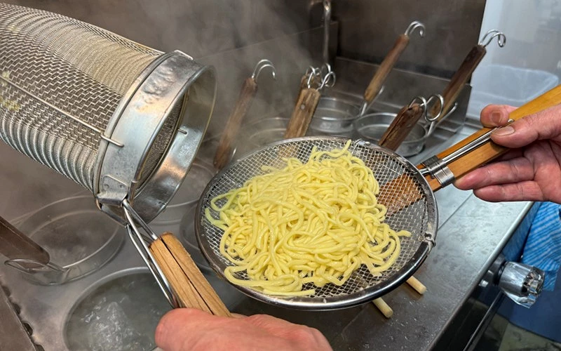 一雙手拿著麵篩將麵倒進瀝水籃中