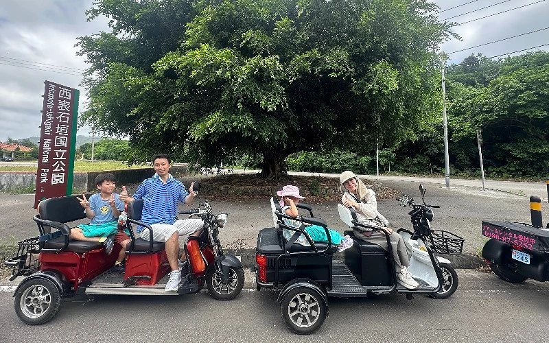 兩台三輪車分別載著兩人,停駐於一棵大樹前