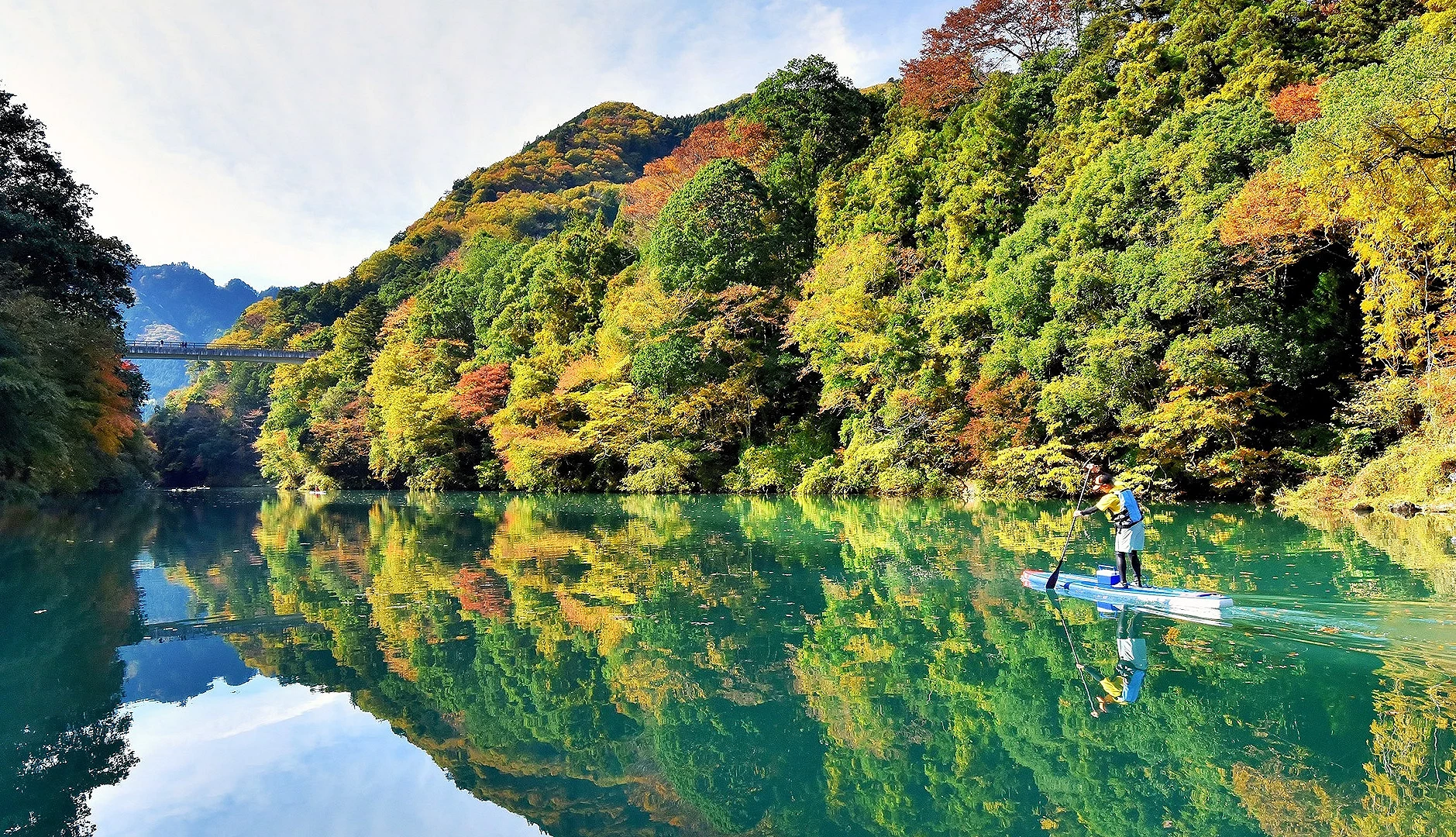 左右兩側是綠黃紅色的樹林,中間有湖,湖上有個人在划船