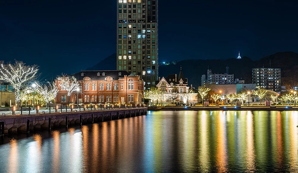 門司港懷舊區夜景,紅磚建築與洋館在燈光照耀下閃爍,水面映出璀璨倒影