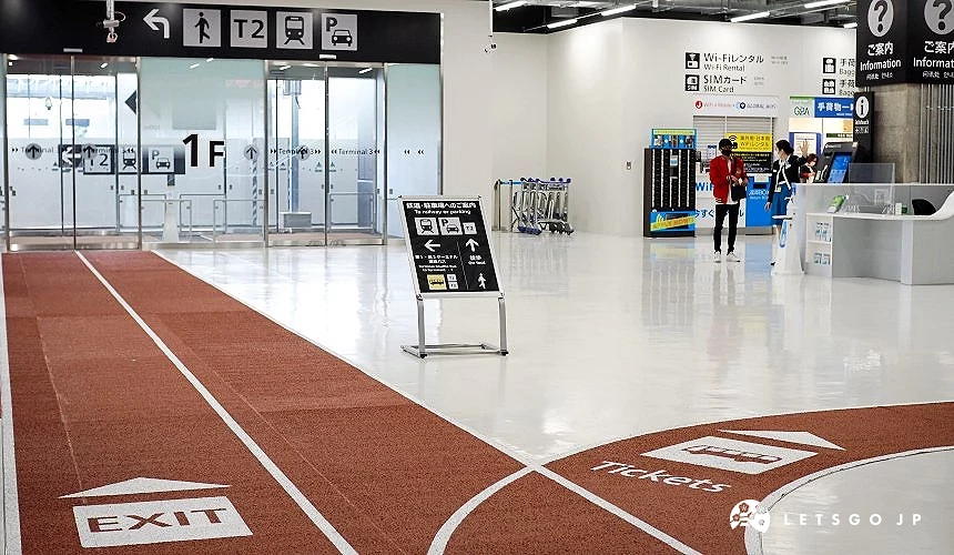 成田機場第三航廈1樓抵達大廳,紅色地面導引線標示「EXIT」與「Tickets」方向,背景可見前往第二航廈及巴士的指標
