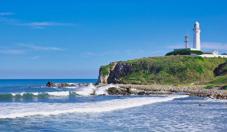 海浪拍打岩岸的太平洋景色,岬角上矗立著白色燈塔。