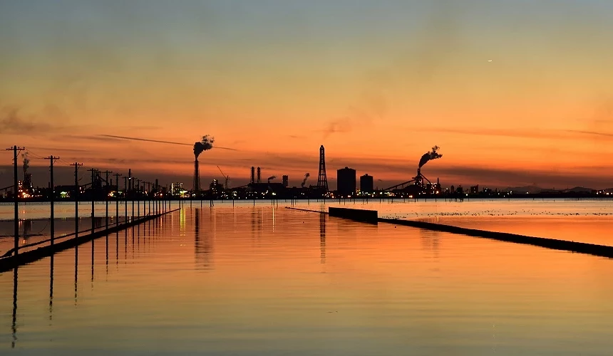 夕陽餘暉下的海上電線桿與工廠煙囪,倒映在水面形成剪影景色。