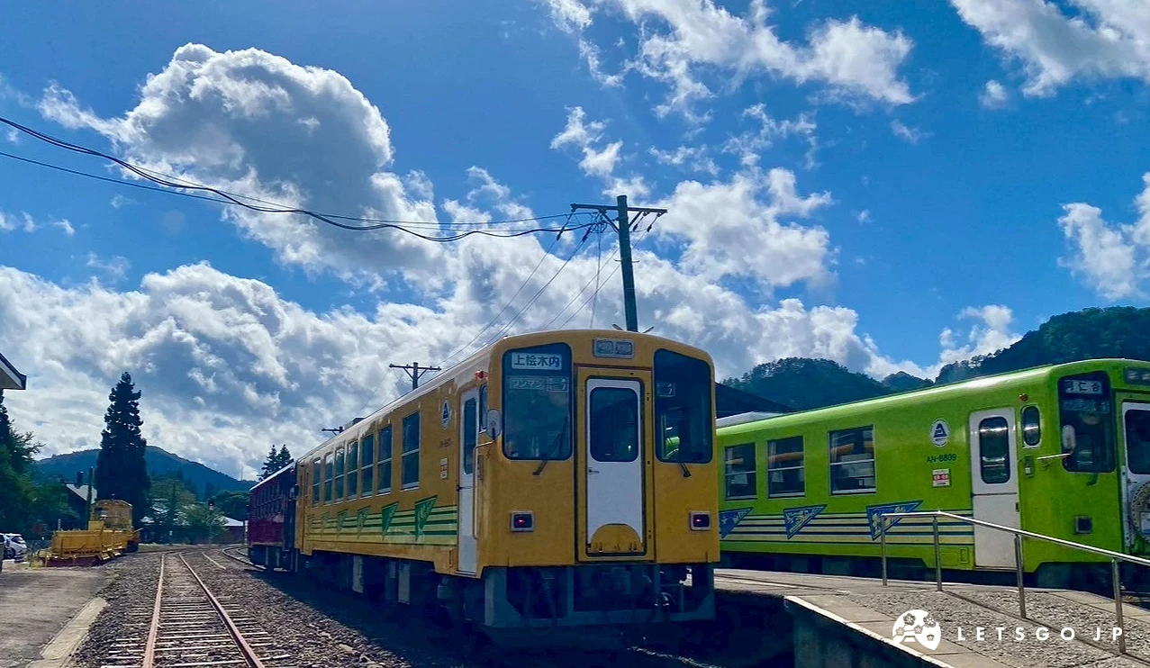 一輛黃色的火車行駛在鄉村鐵軌上,背景是綠色樹林和藍天。