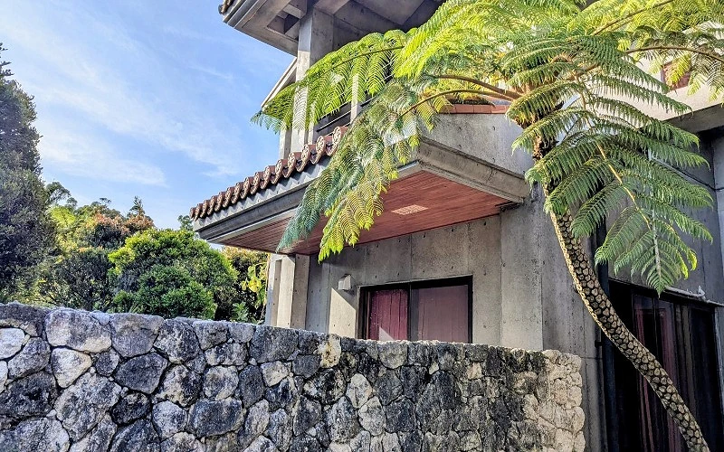 灰色石牆與混凝土建築外觀,屋簷下有紅瓦與樹蕨