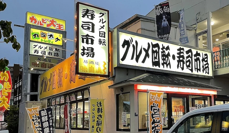 迴轉壽司市場店面白底黑色書法字的招牌,店門口版放眾多旗幟
