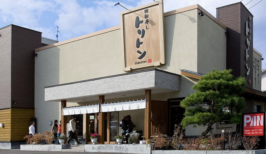TORITON 迴轉壽司店舖,淺色調為主的獨棟建築,木質的招牌寫這黑色書法字體的logo