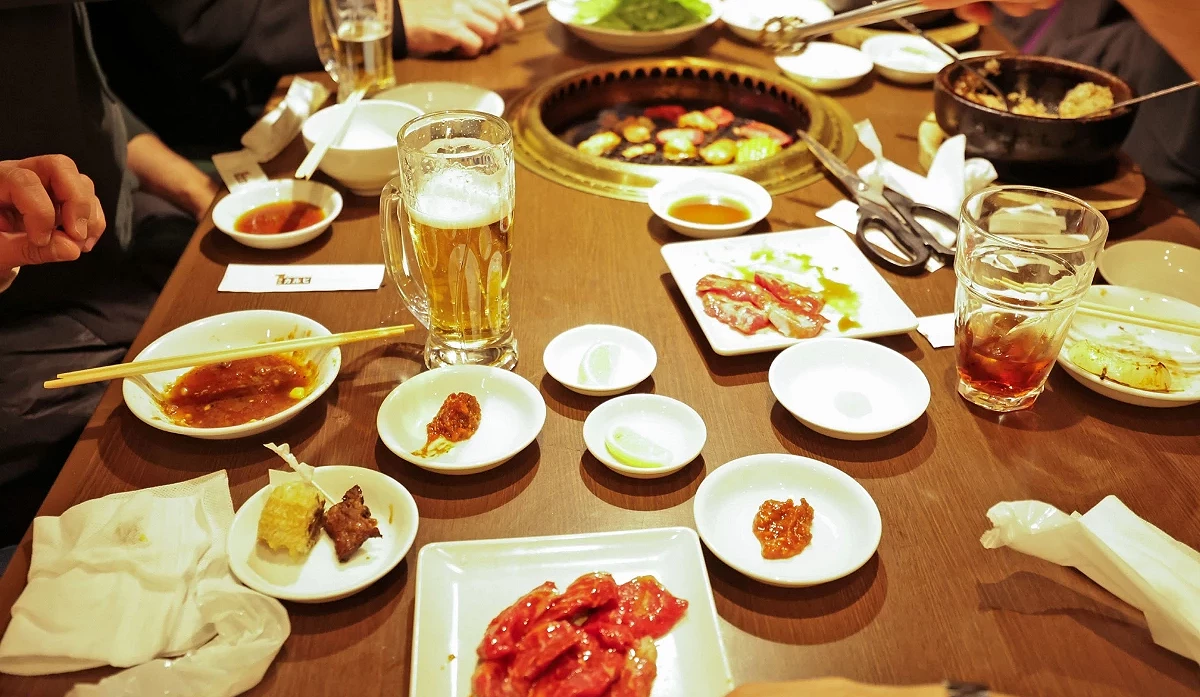 一張居酒屋的餐桌俯視圖,上面擺滿了多個小碟子,裝著各種日式開胃菜和一杯啤酒。