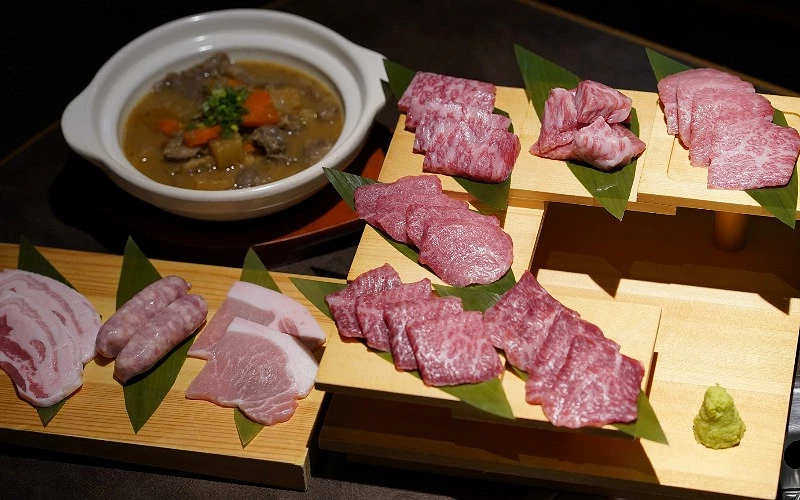 多層木盤上擺放石垣牛牛肉與豬肉片,後方有燉菜料理
