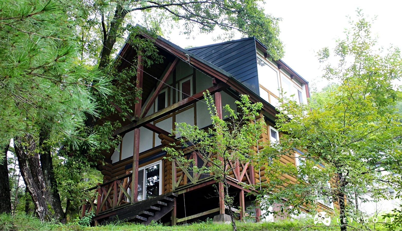 山坡上紅棕色木造小屋,外牆與欄杆結構明顯,周圍為樹林