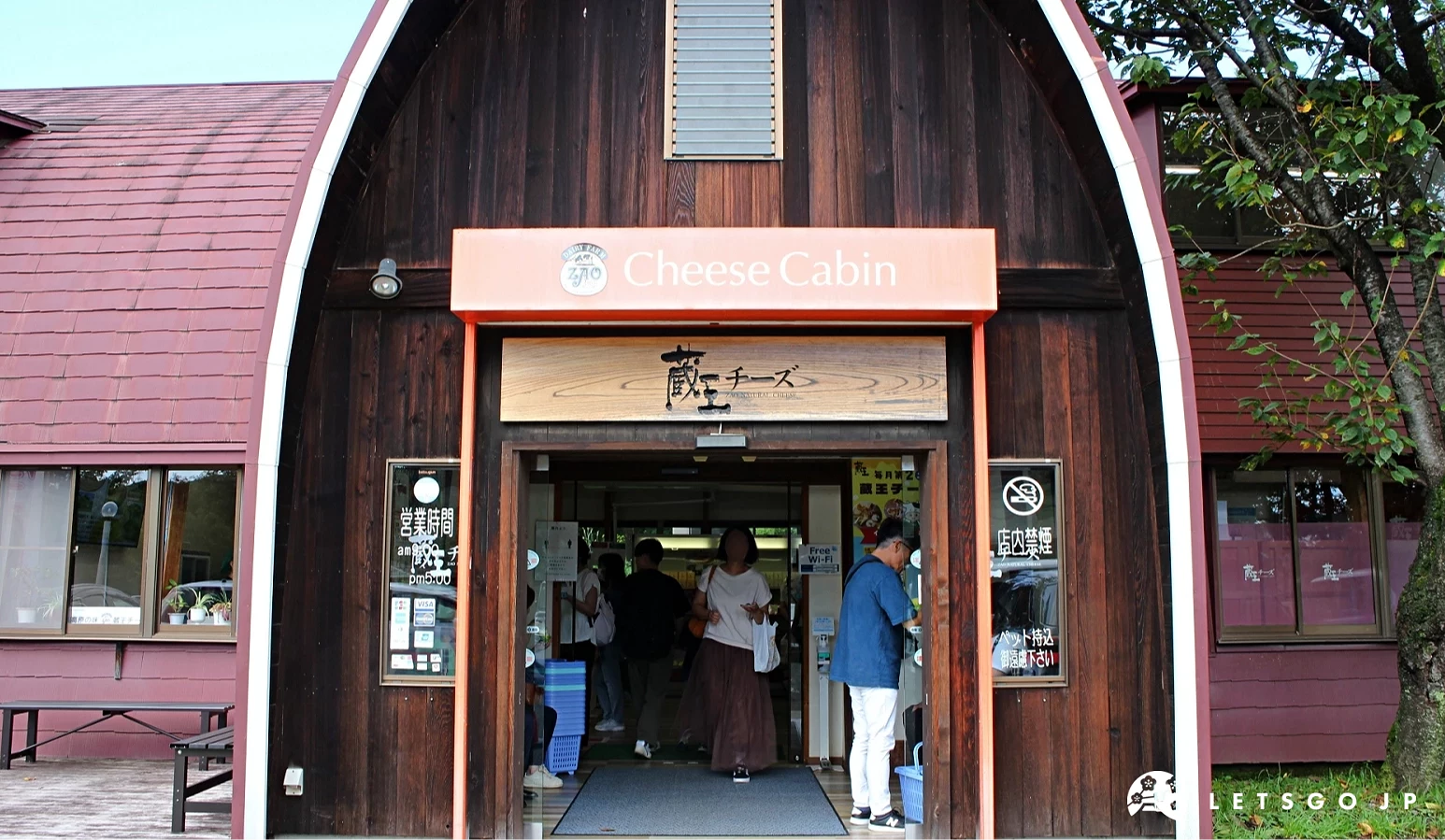 寫有「Cheese Cabin」與「藏王チーズ」的木造拱形店舖入口,民眾進出其間