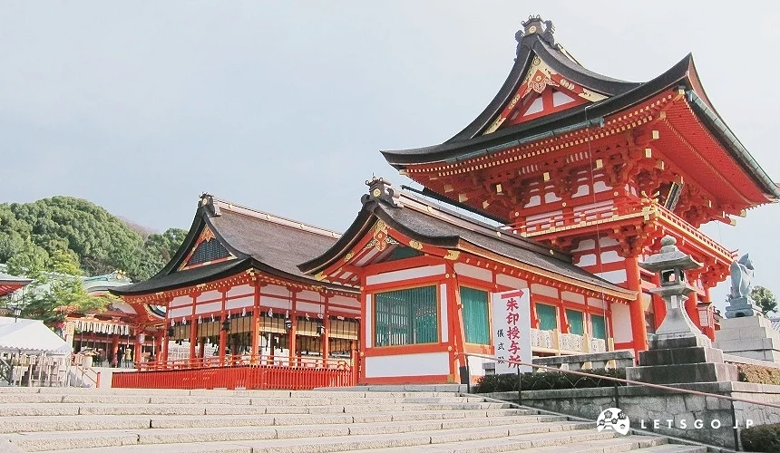 伏見稻荷大社的本殿,朱紅色神社建築與屋簷細節清晰可見,前方為石階,背景為綠意山景