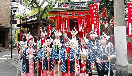 身著和服與法被、臉上化有狐狸妝容的參與者站在王子稻荷神社前,周圍可見成排的紅色旗幟