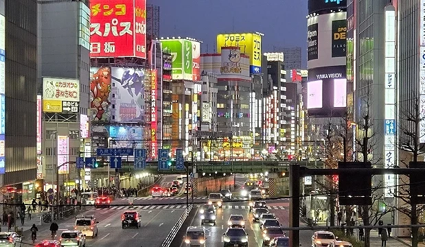 夜晚的東京街區燈光明亮,車流與行人穿梭其間,部分店家看板依舊亮起