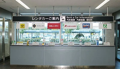 大分機場內部的租車資訊櫃台,櫃檯上方有多家租車公司的標誌,玻璃窗後方可見停車場與外部景色